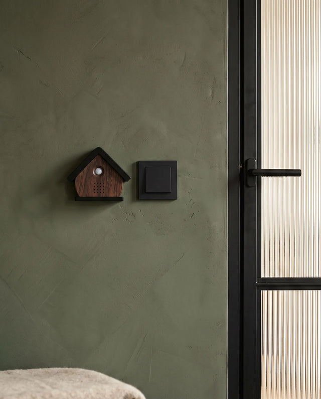 Het vogelhuisje in Walnoot aan een olijfgroene muur in de gang, naast de lichtschakelaar